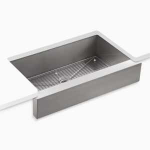 A stainless steel farmhouse kitchen sink installed under a countertop. It features a rectangular shape with a grid rack at the bottom to protect the surface, along with a central drain hole. The countertop is white, contrasting with the metallic sink.