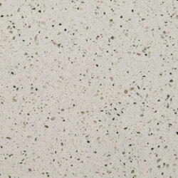 A close-up of a terrazzo surface with a beige background. It features small, irregularly shaped flecks in shades of gray, brown, and black, creating a speckled, textured appearance.