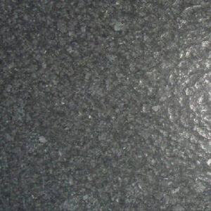 Close-up of a dark gray, textured stone surface with a rough pattern. The light reflects on the right side, highlighting the grainy details and uneven surface texture.