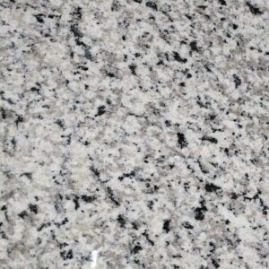 Close-up of a polished granite countertop with a speckled pattern. The surface has a mix of light gray, white, and black colors, creating a mottled effect typical of natural stone. The texture is smooth with a subtle shine.